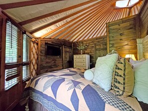 A cozy room with a bed, wooden walls, and a window with blinds. - Group 05) Spring Ridge Yurt (Topton)