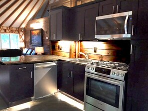 Una cocina con armarios oscuros, una estufa de acero inoxidable, un microondas y un lavavajillas.