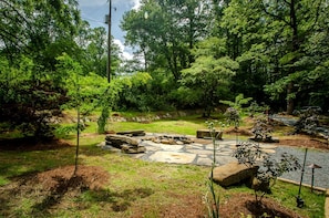 A stone fire pit surrounded by a grassy area with trees in the background. - Group 05) Spring Ridge Yurt (Topton)