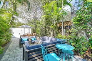 Une terrasse extérieure dotée d’un espace salon, comprenant un canapé et des fauteuils, entourée d’une végétation luxuriante et d’une plateforme en bois.