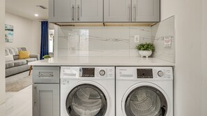 Une buanderie moderne avec deux machines à laver à chargement frontal, un meuble gris au-dessus et une petite plante en pot posée sur le plan de travail.