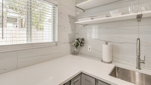 Une cuisine moderne dotée de plans de travail en marbre blanc, d’un évier en acier inoxydable et d’étagères intégrées pour ranger la vaisselle.