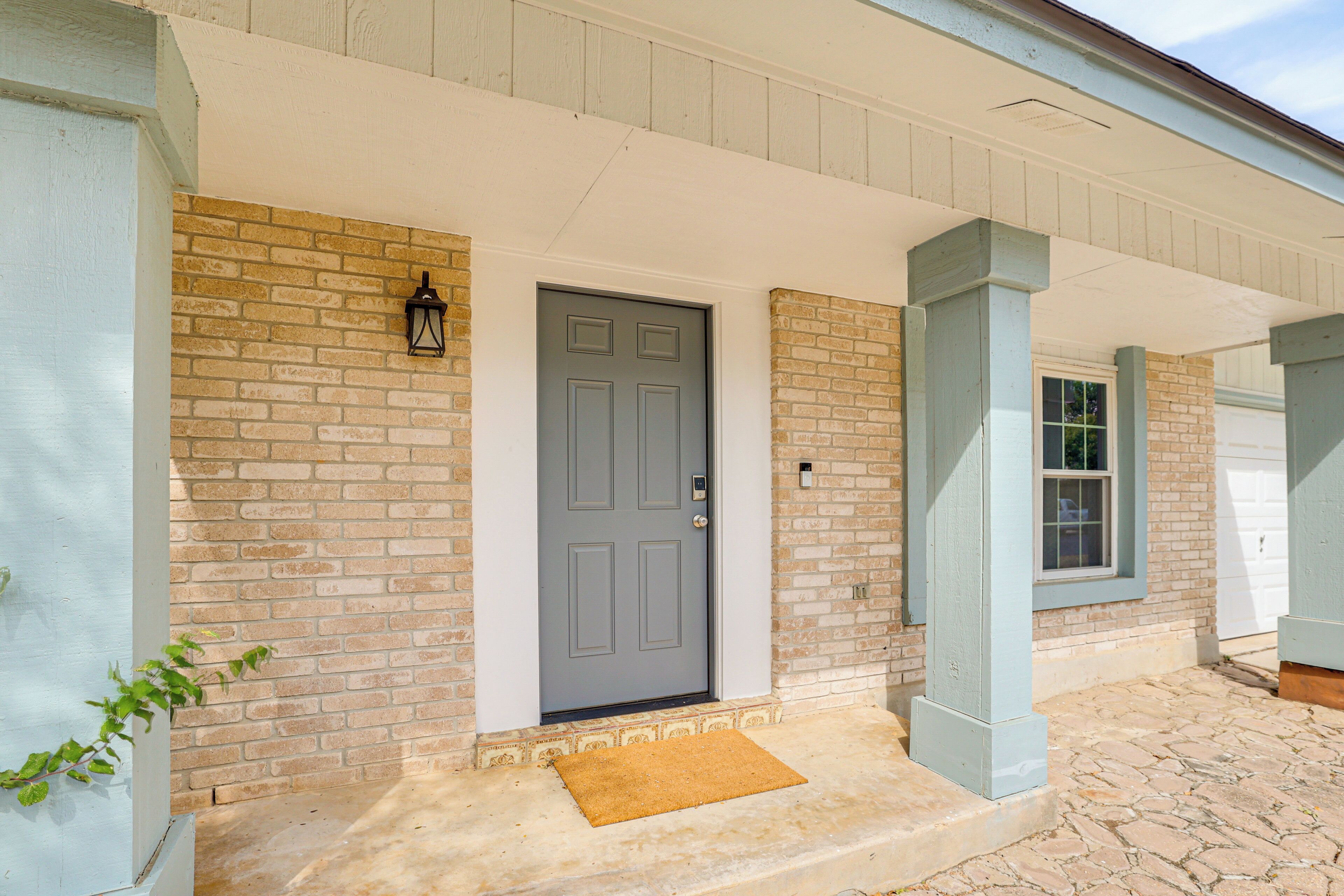 A house with a gray front door, a brick wall, and a stone-paved entrance.