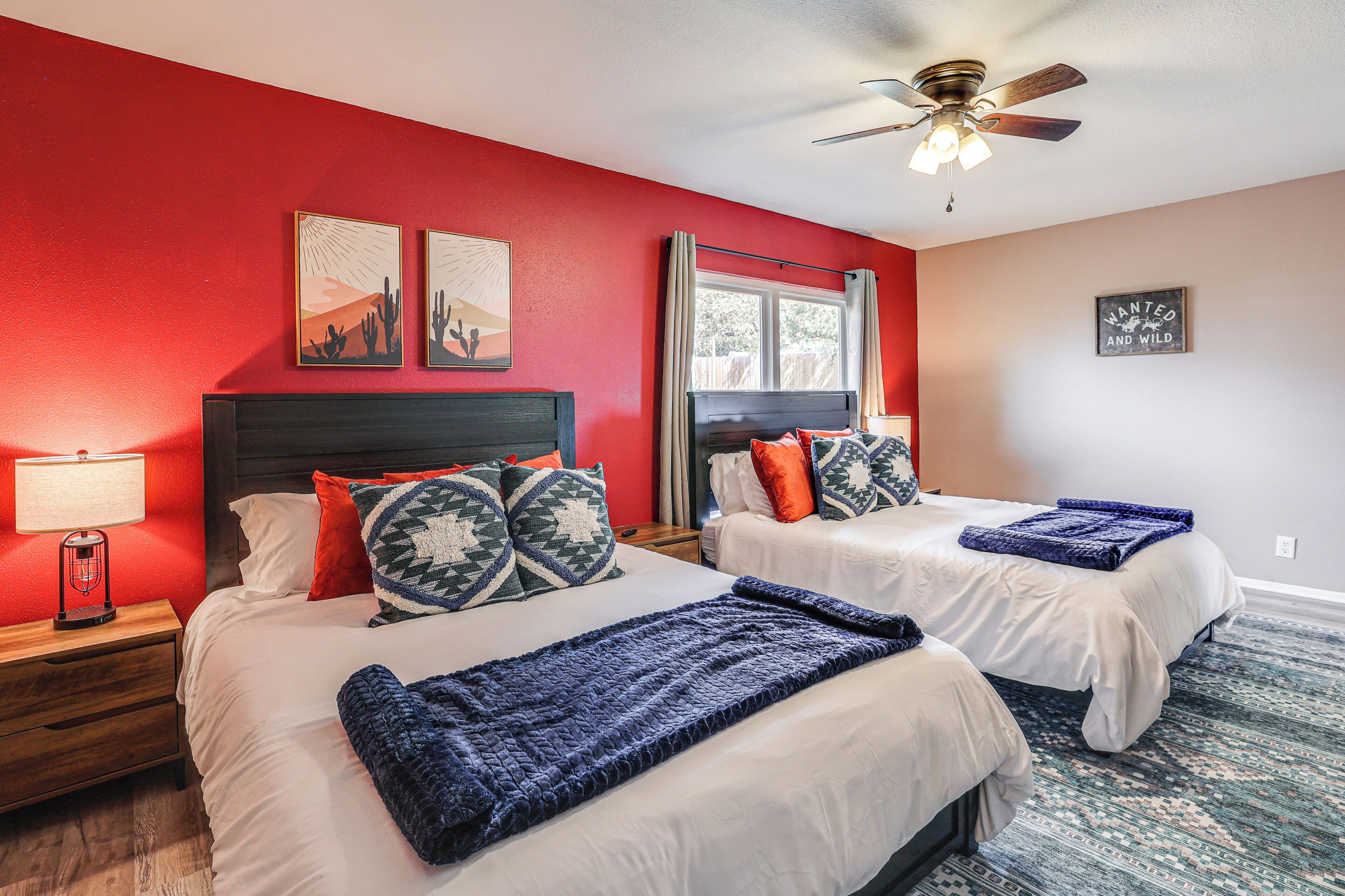 A hotel room with two beds, red walls, a ceiling fan, and artwork on the walls.