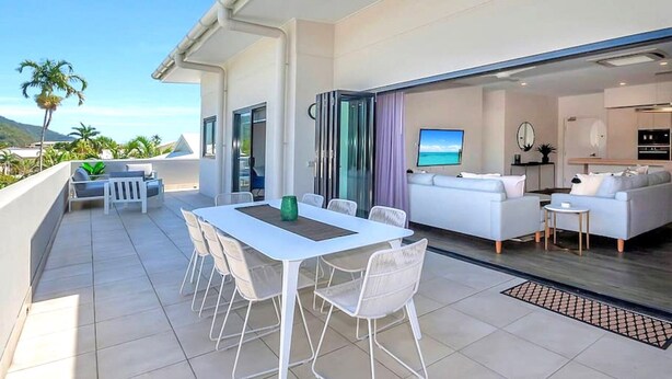 A modern outdoor patio with a dining table and chairs, a sofa, and a TV in the living area.