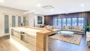 A modern kitchen with a central island, a dining area with a sofa and coffee table, and a large window with curtains.