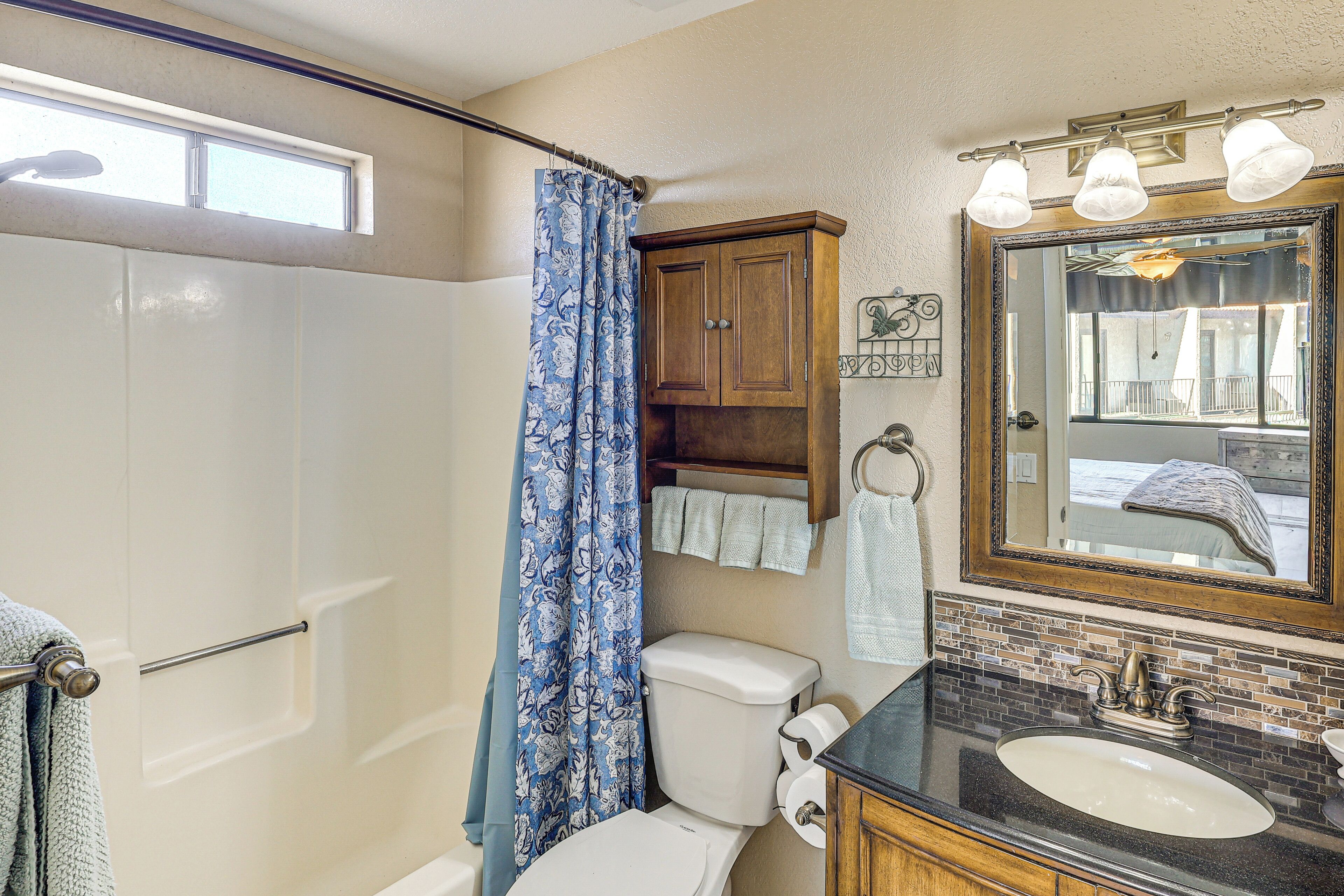 A bathroom with a shower, toilet, sink, and a large mirror with lights.