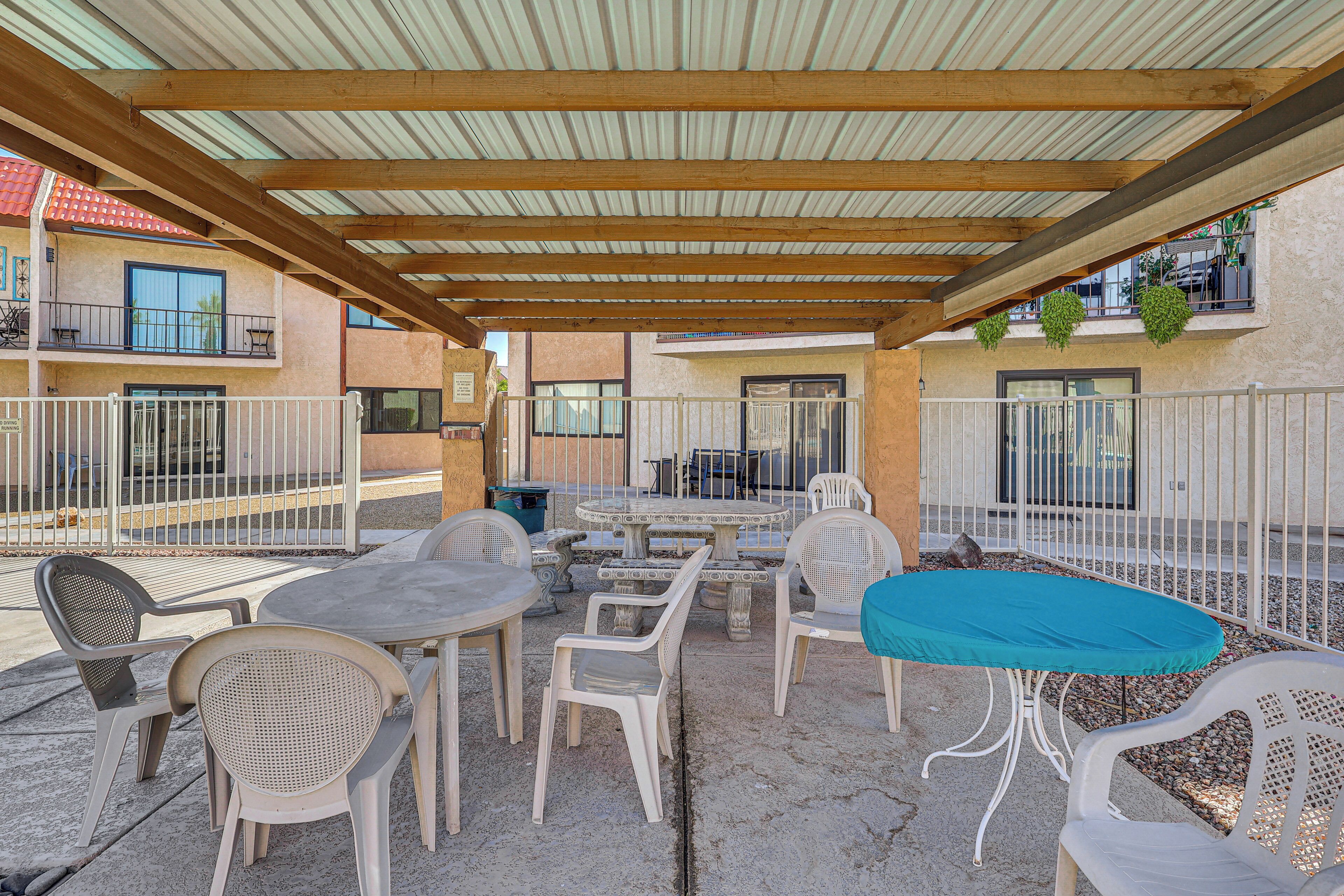 Un patio exterior con mesas y sillas, una zona cubierta con techo de madera y vistas a edificios cercanos.