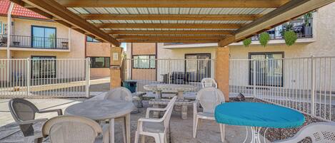 Un patio exterior con mesas y sillas, una zona cubierta con techo de madera y vistas a edificios cercanos.