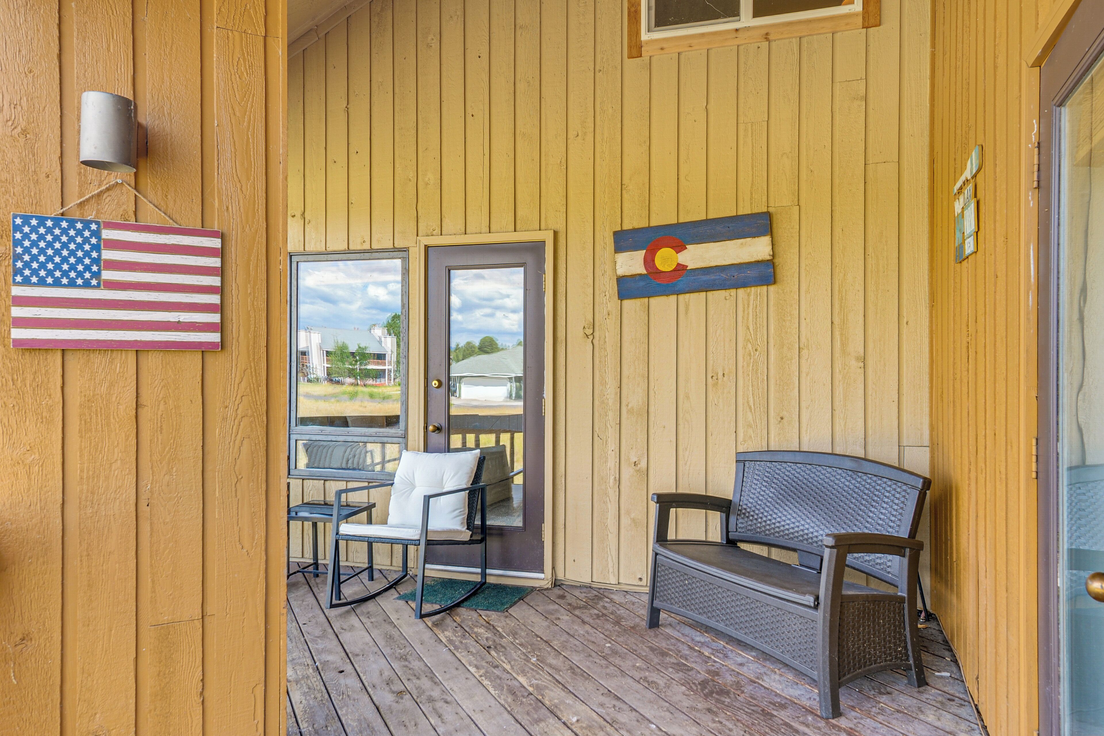 A wooden porch with a bench, two doors, and flags.