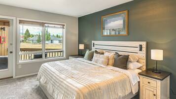 A bedroom with a large bed, a nightstand, a lamp, a window with a view of a house and trees, and a framed picture on the wall.