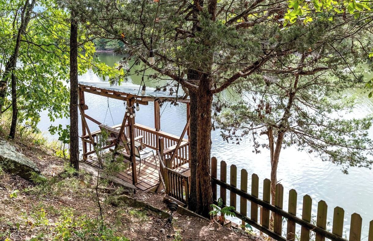 Una terraza de madera con un columpio, con vistas a un lago tranquilo, rodeada de árboles.