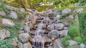 A small waterfall cascading over rocks in a garden setting. - Upscale Group Getaway in Orem w/ Private Hot Tub (Orem)