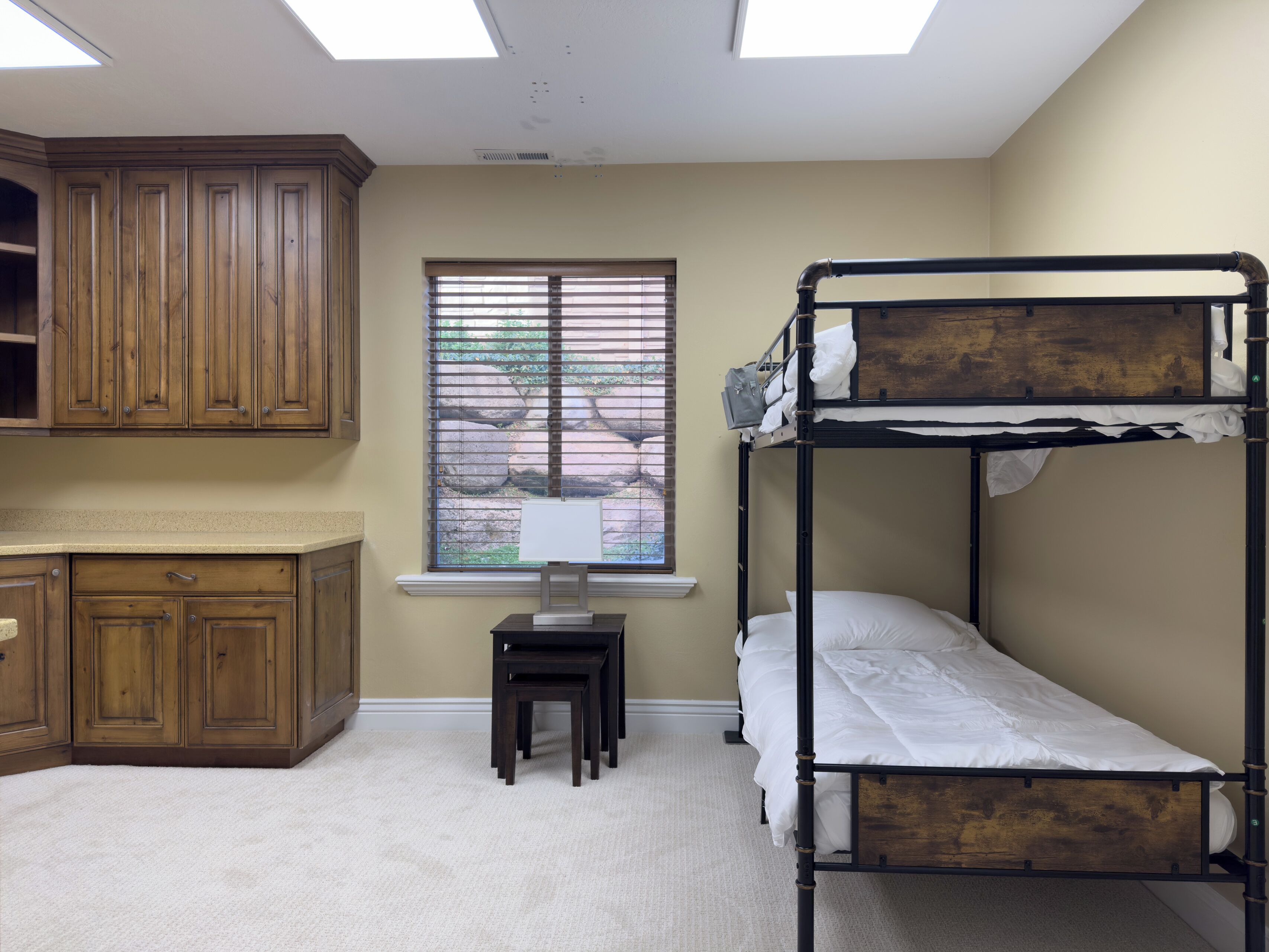 A bunk bed with a desk and chair, wooden cabinets, a window with blinds, and a skylight.