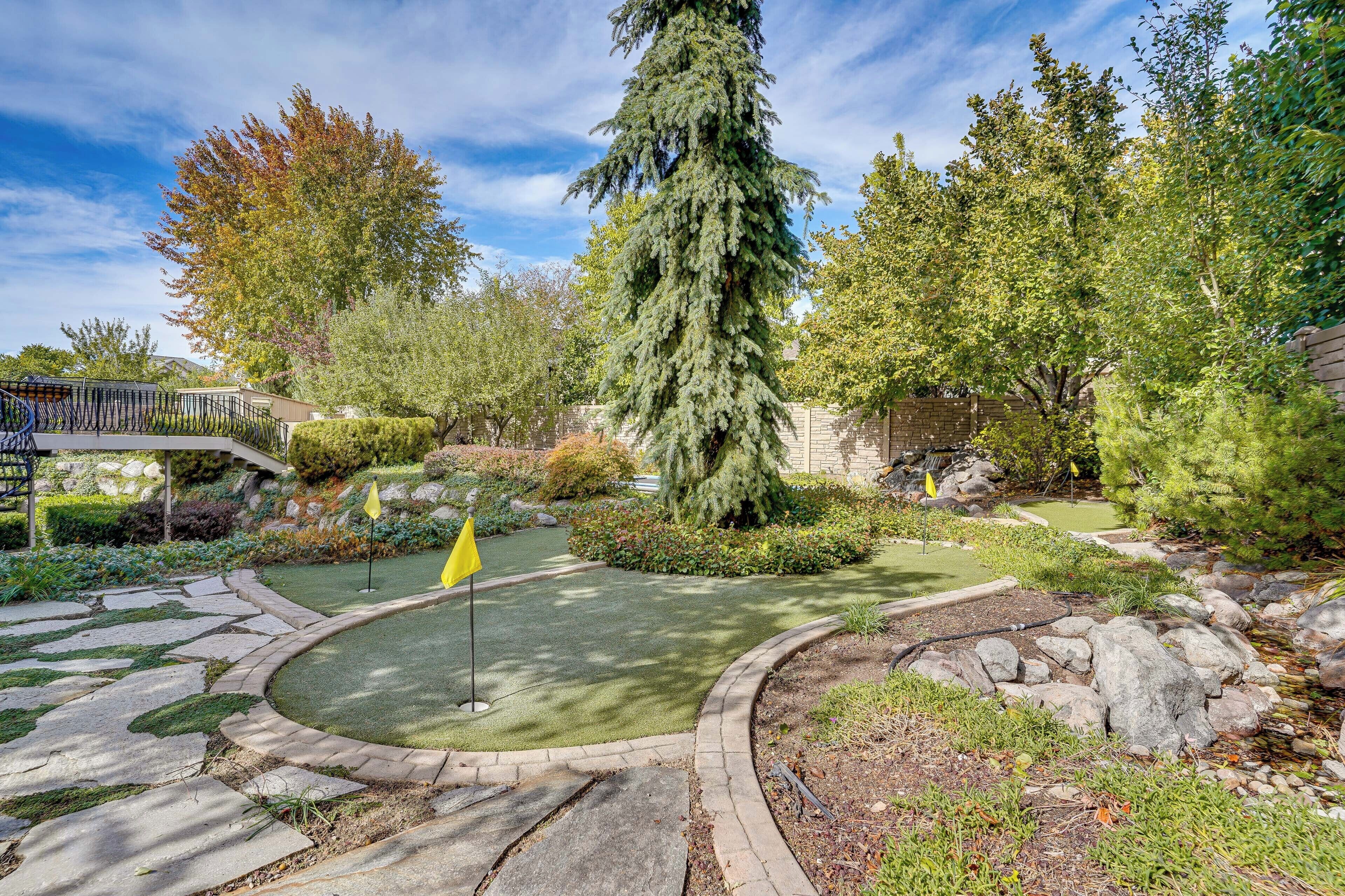 A landscaped garden with a putting green, stone pathways, and various trees.
