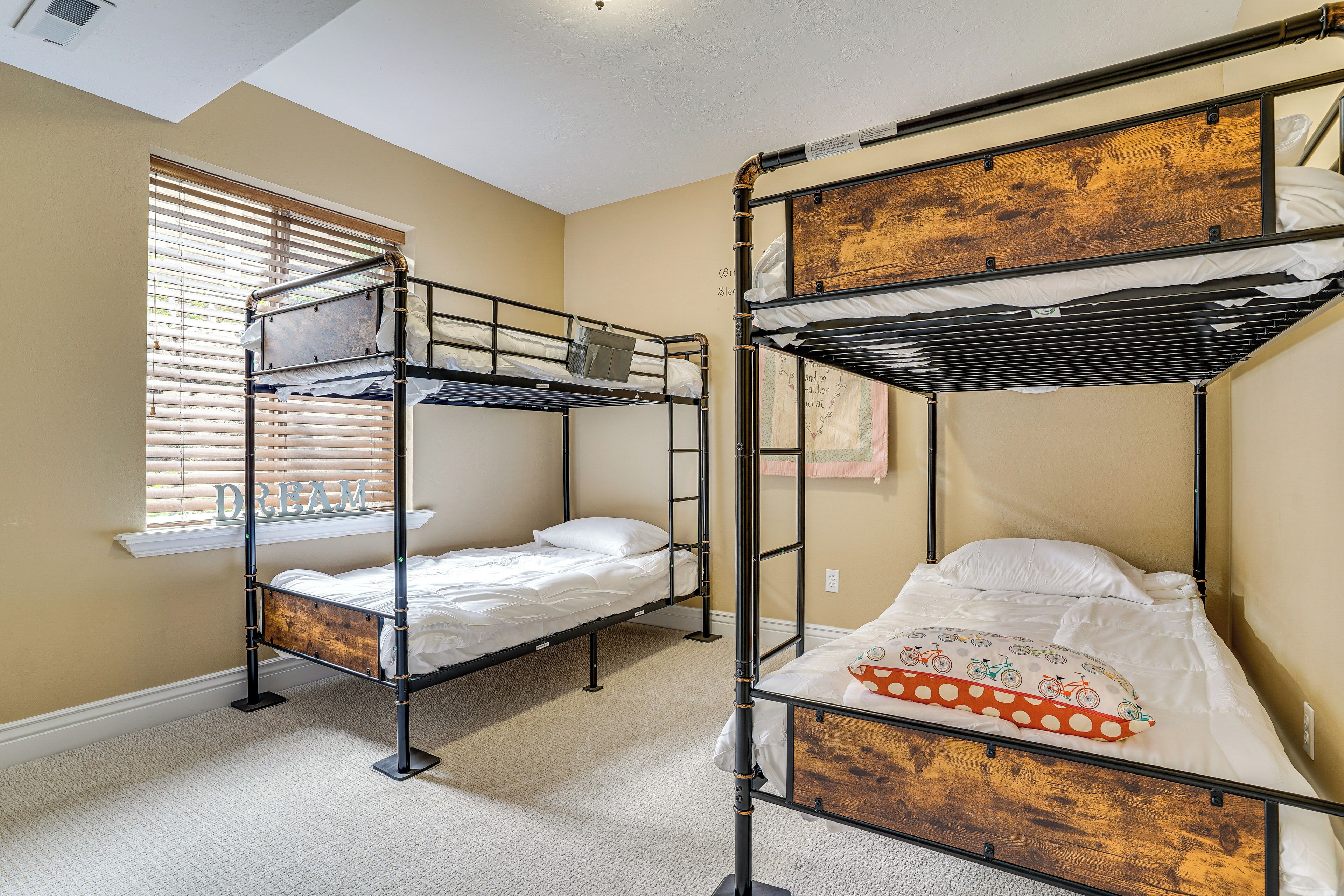 A room with two bunk beds, a window with blinds, and a carpeted floor.