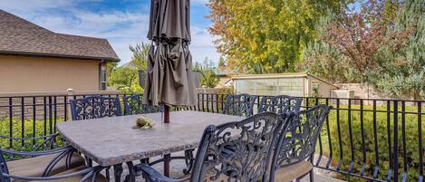 Eine Terrasse mit Tisch und Stühlen, einem Sonnenschirm und Blick auf ein Haus und Bäume.