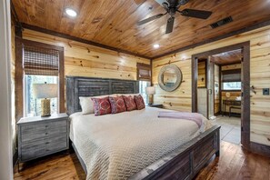 A wooden-paneled bedroom with a bed, nightstands, a ceiling fan, and a window with blinds. - Creekside Cabin Perfect for Family Getaways in Broken Bow, Oklahoma (Broken Bow)
