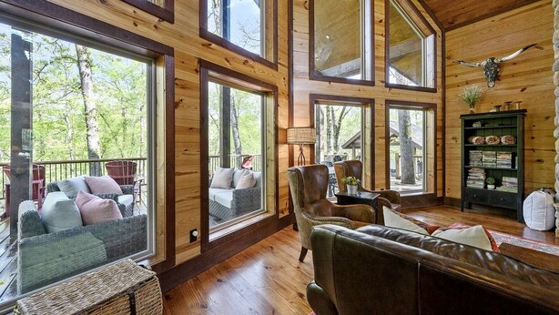 A spacious wooden interior with large windows, a leather sofa, and a bookshelf. - Creekside Cabin Perfect for Family Getaways in Broken Bow, Oklahoma (Broken Bow)