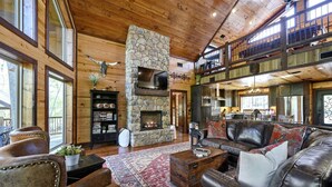 A spacious living room with a stone fireplace, leather furniture, and a balcony overlooking the landscape. - Creekside Cabin Perfect for Family Getaways in Broken Bow, Oklahoma (Broken Bow)