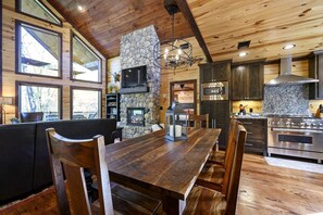 A wooden interior with a stone fireplace, a dining table, and modern kitchen appliances. - Creekside Cabin Perfect for Family Getaways in Broken Bow, Oklahoma (Broken Bow)