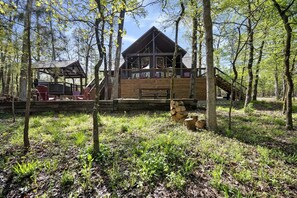 Une cabane dotée d’une terrasse, entourée d’arbres et bordée d’une zone herbeuse.
