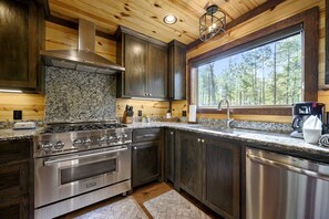 A modern kitchen with granite countertops, stainless steel appliances, and a large window offering a view of trees. - Creekside Cabin Perfect for Family Getaways in Broken Bow, Oklahoma (Broken Bow)