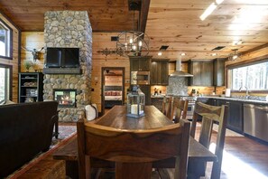 Un intérieur en bois avec une cheminée en pierre, un coin repas avec des chaises, une cuisine dotée de plans de travail en granit et un mur en pierre.