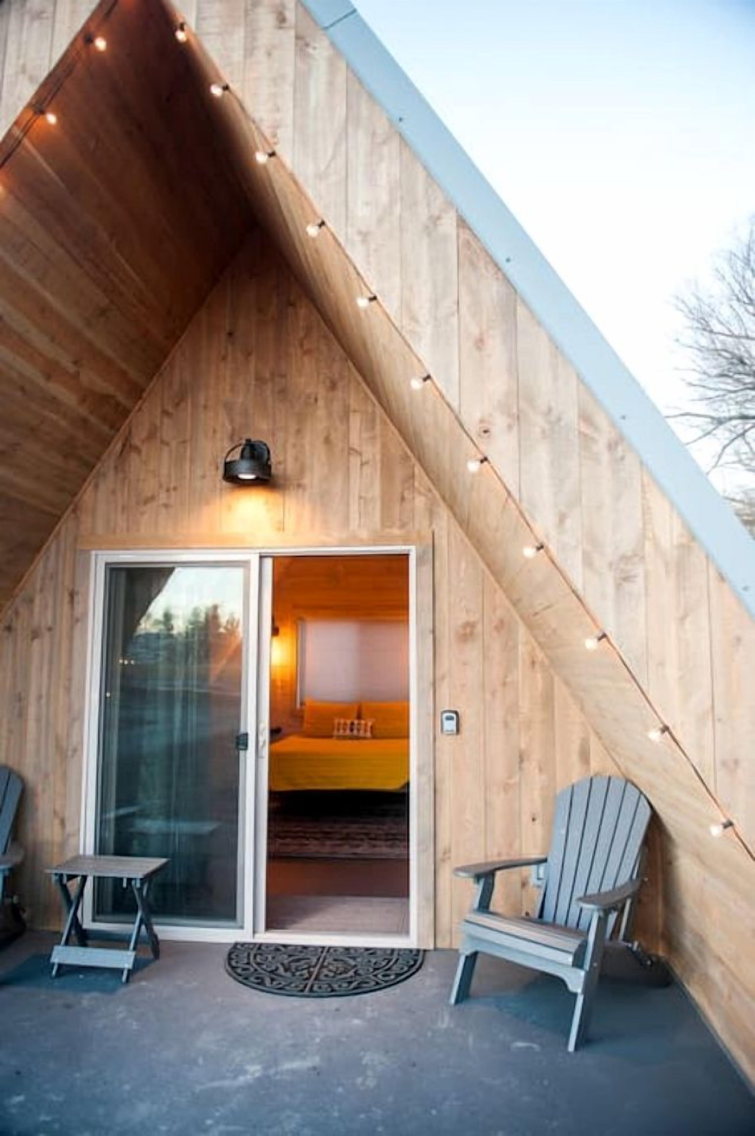 Une cabane en bois avec un toit en pente, une porte d’entrée en verre, deux fauteuils Adirondack et une petite marche menant à la porte.