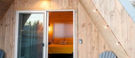 Une cabane en bois avec un toit en pente, une porte d’entrée en verre, deux fauteuils Adirondack et une petite marche menant à la porte.