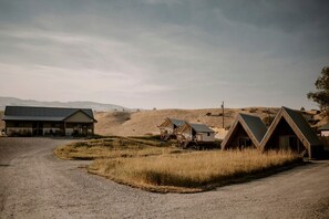 Un entorno rural con un camino de grava, una construcción grande tipo granero y varias cabañas con techo triangular.