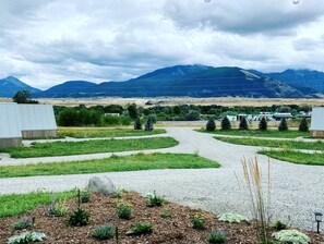 Un camino de grava conduce a un edificio de diseño moderno, rodeado de zonas ajardinadas y montañas a lo lejos.