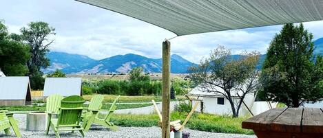 Ein überdachter Sitzbereich im Freien mit Picknicktisch, grünen Stühlen und Bergblick.