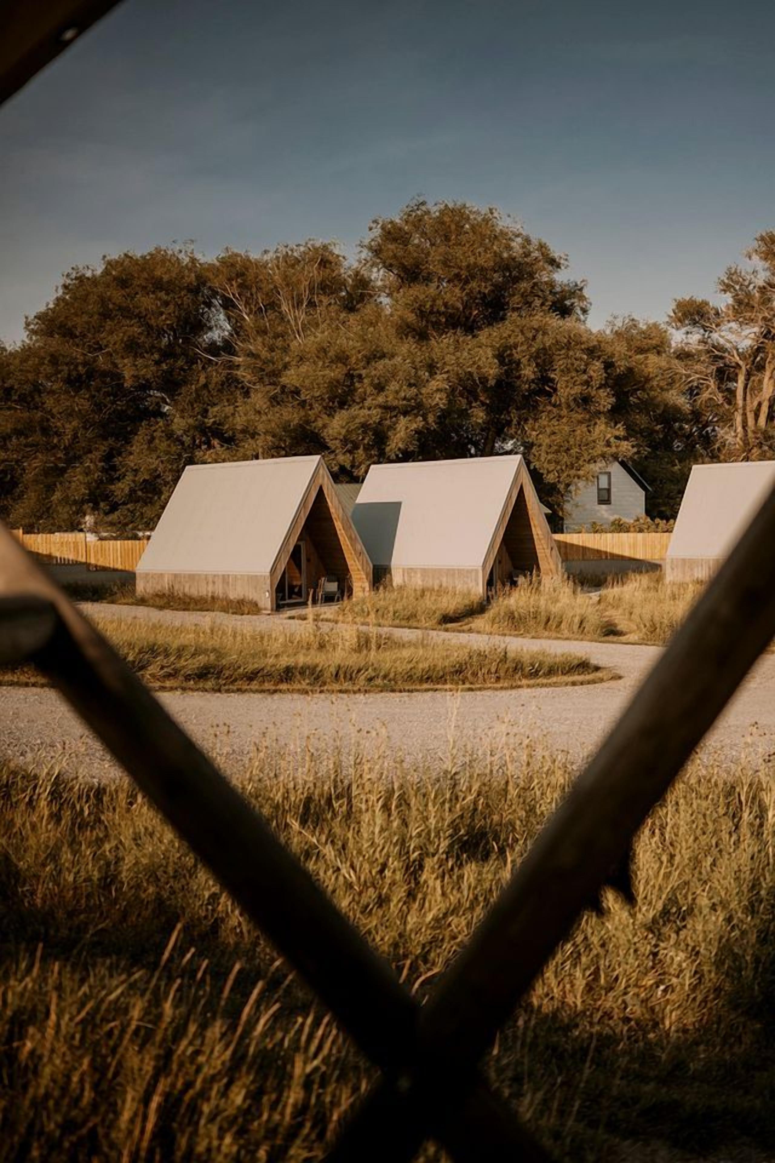 A series of triangular-roofed cabins in a natural setting with trees in the background.