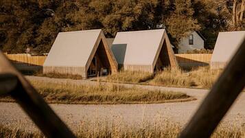 A series of triangular-roofed cabins in a natural setting with trees in the background.