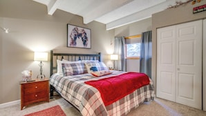 A bedroom with a bed, nightstand, two bedside lamps, a red throw blanket, a plaid bedspread, a framed artwork, and a door with a sign. - Ski Copper Mountain! Alpine-chic Condo w/ Hot Tub (Copper Mountain)