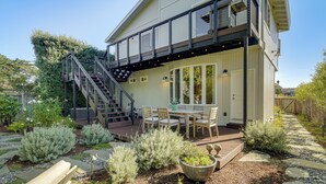 Ein zweigeschossiges Haus mit einem Balkon, einer Terrasse mit Gartenmöbeln und einem Garten mit verschiedenen Pflanzen und einem großen Pflanzgefäß.