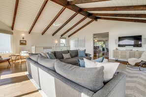 A spacious living room with a large sectional sofa, wooden beams on the ceiling, a flat-screen TV, and a view of the outdoors. - Steps to Ocean: Luxe Family Home in Half Moon Bay! (Half Moon Bay)