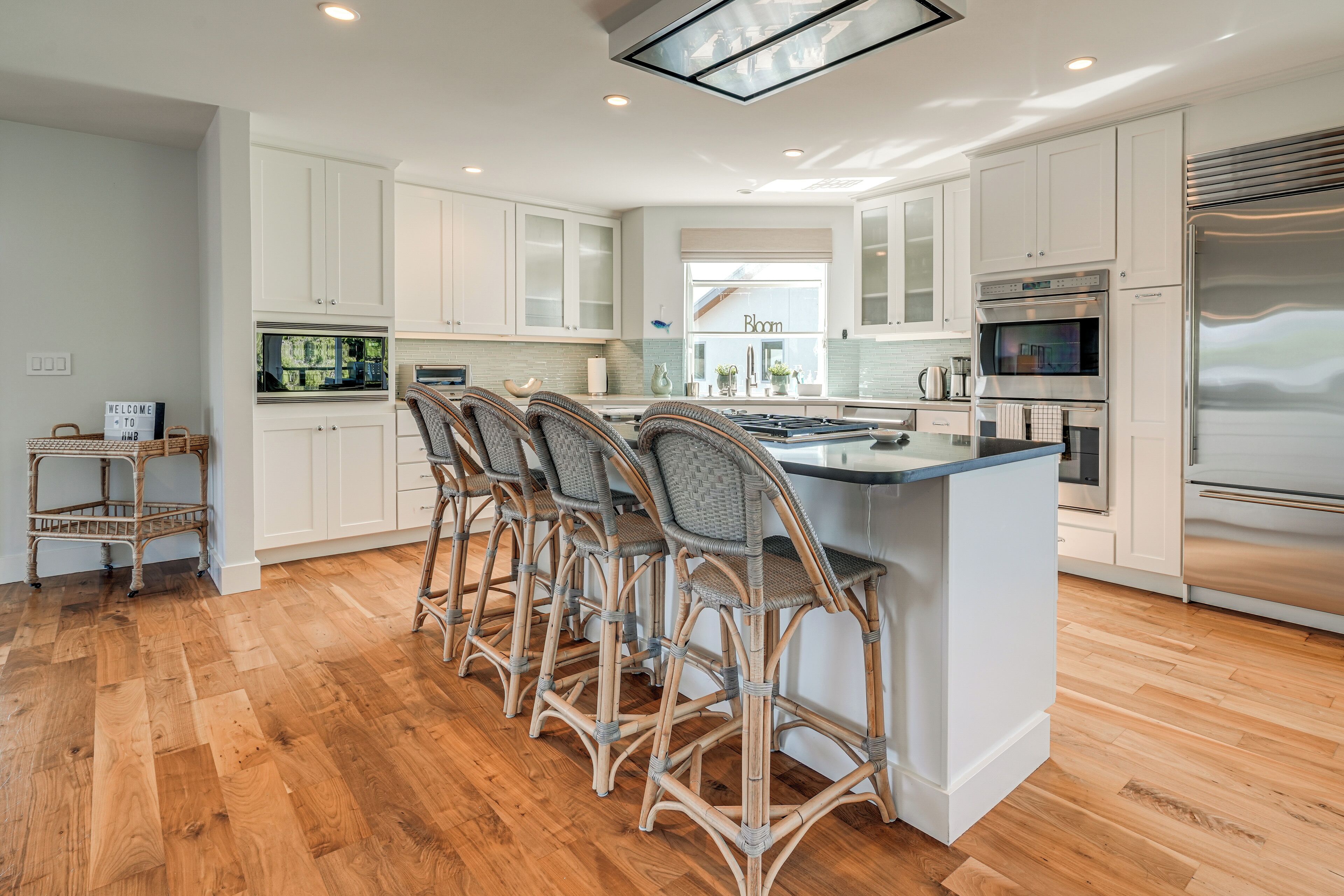 A modern kitchen with white cabinetry, a central island with bar stools, and stainless steel appliances.
