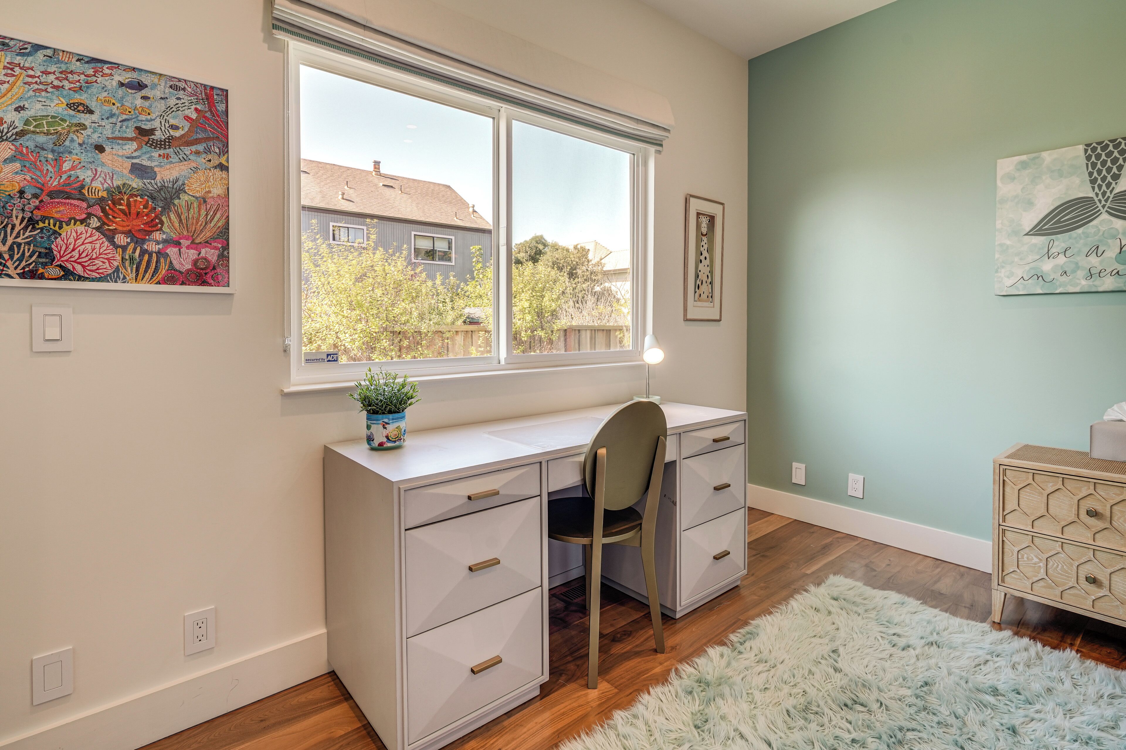 Une pièce comprenant un bureau, une chaise et une fenêtre donnant sur une maison.
