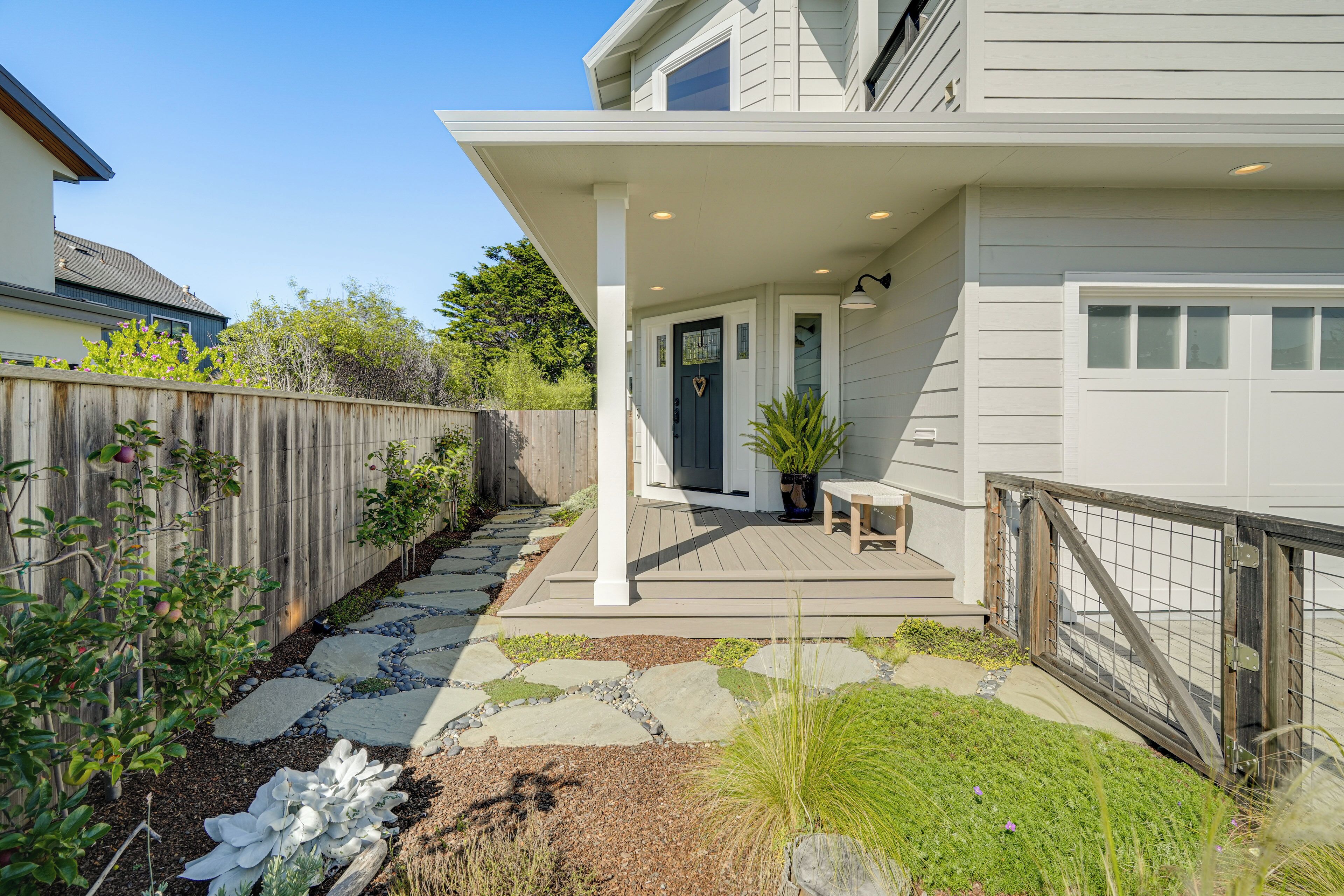 A modern house with a covered porch, a stone pathway, and a fenced backyard.