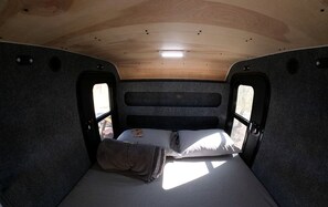 Ein kompaktes Wohnmobil-Interieur mit einem Einzelbett, einem kleinen Tisch und einem Fenster.