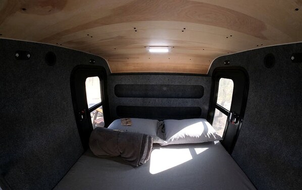 A compact RV interior with a single bed, a small table, and a window.