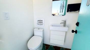 A small bathroom with a toilet, a sink, and a sign indicating sensitive plumbing.
