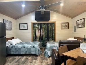 A room with two beds, a dining table, a ceiling fan, and a TV. - Dream Glamping in Texas in this Cozy, Pet-Friendly Cabin in Bastrop, TX (Bastrop)