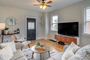 A living room with a ceiling fan, a television on a wooden cabinet, and a door with a mirror. - Pet-friendly Oakley Gem w/ Large Backyard! (Cincinnati)