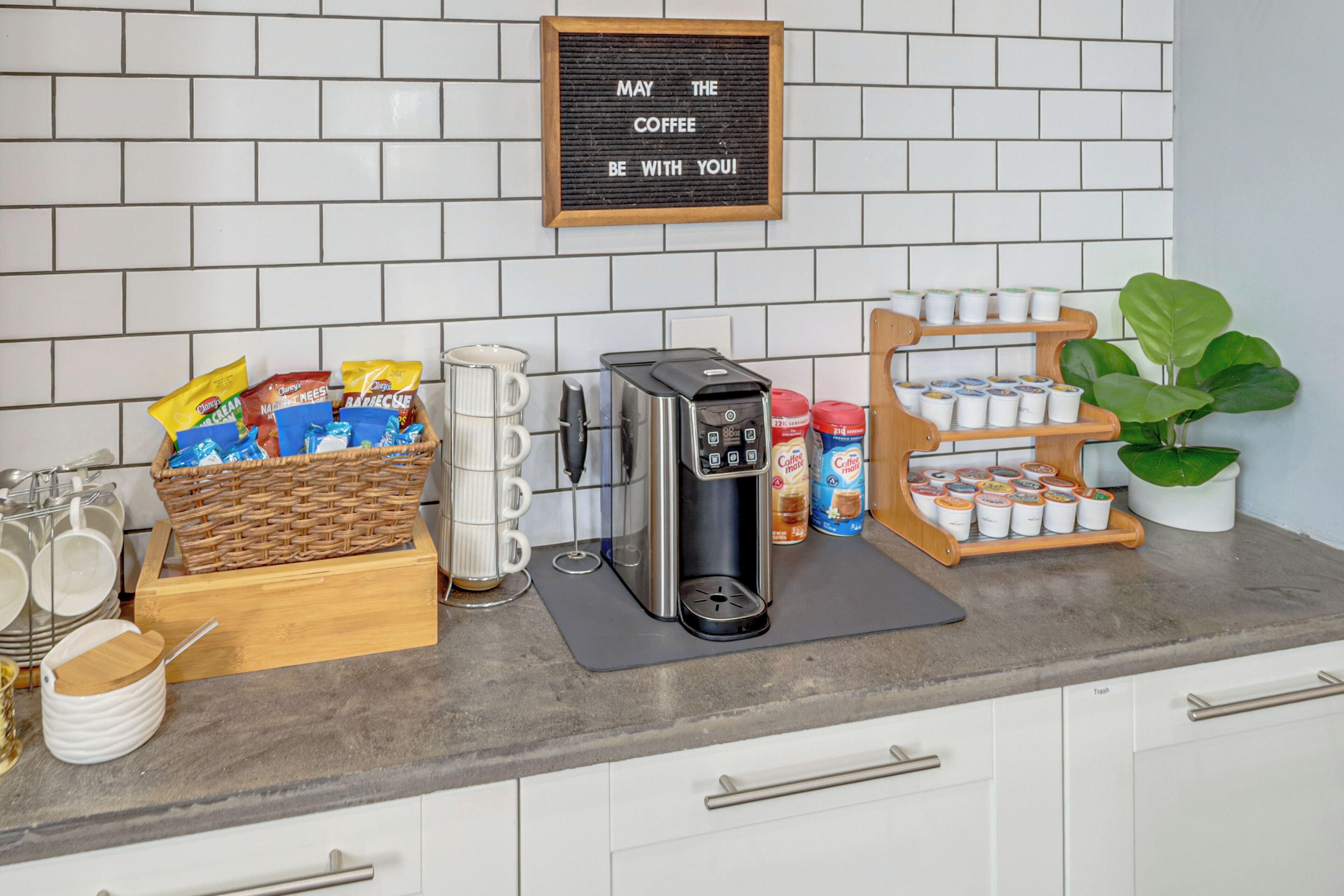 A kitchen area with a coffee station, including a coffee maker, cups, and coffee pods.
