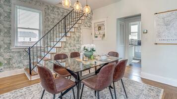 Un comedor con mesa de vidrio, sillas de cuero, una escalera y una pared con estampado floral.