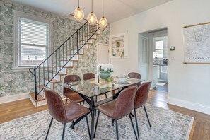 A dining area with a glass table, leather chairs, a staircase, and a wall with a floral pattern. - Pet-friendly Oakley Gem w/ Large Backyard! (Cincinnati)