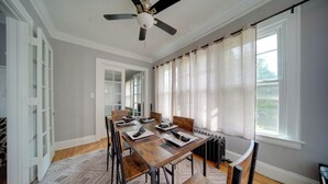 A dining room with a wooden table set for six, a ceiling fan, and a view of the outdoors through large windows. - Deck, Pool Table! Walkable Cleveland Heights Apt (Cleveland Heights)